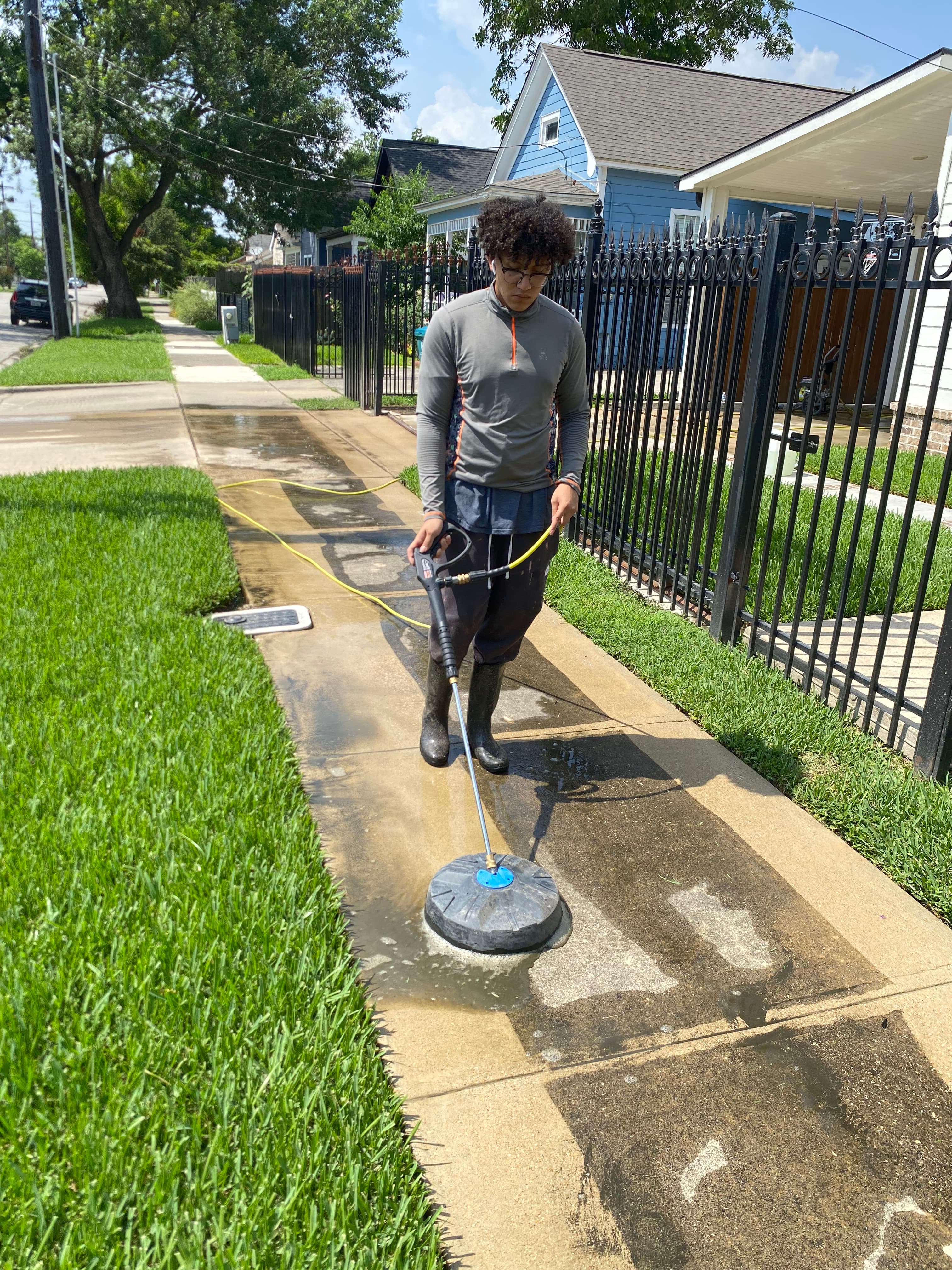 Person using a surface cleaner attachment to pressure wash a dirty concrete sidewalk.