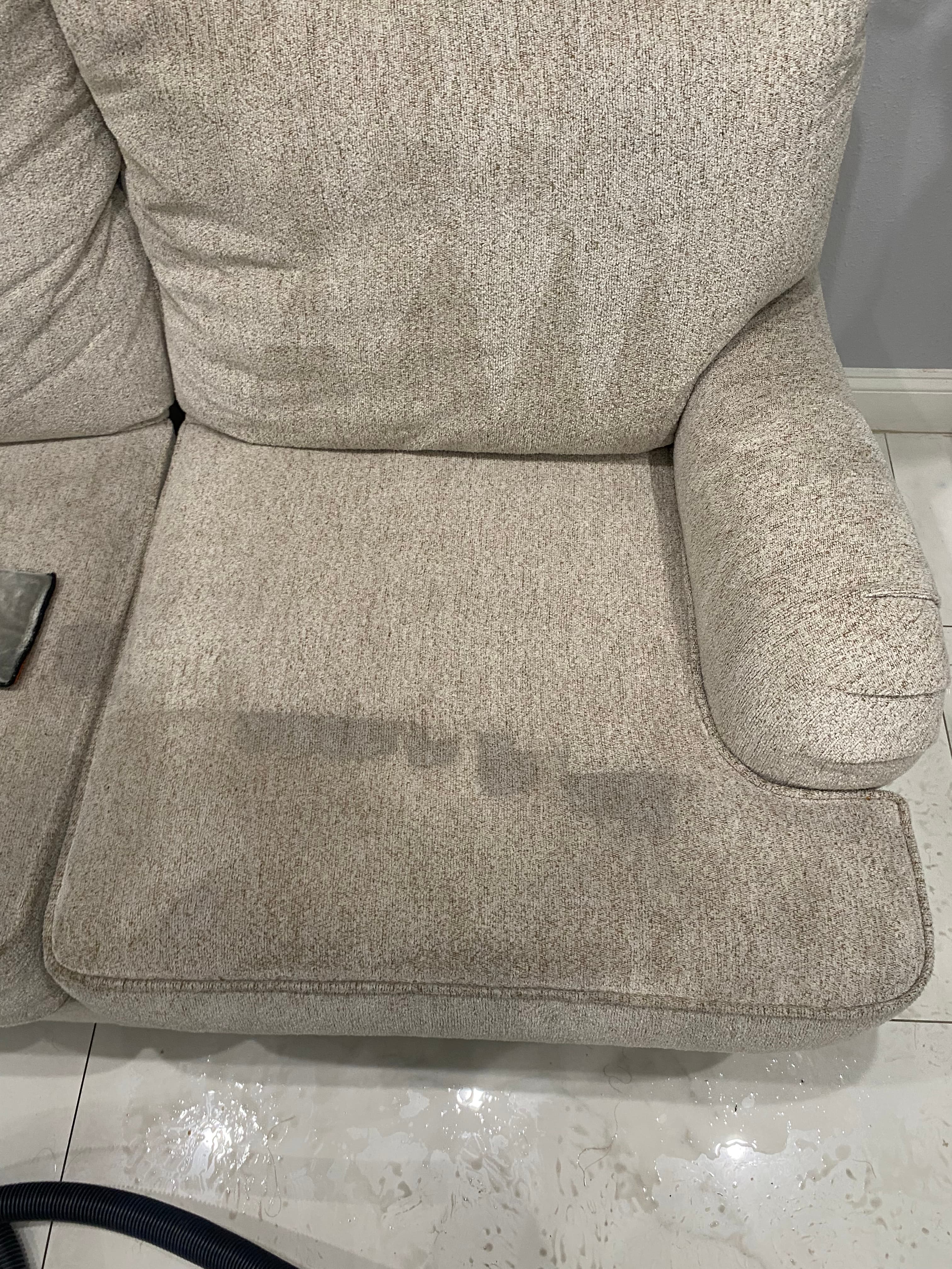 Large dark wet stain on a beige textured sofa cushion next to wet tiled floor.