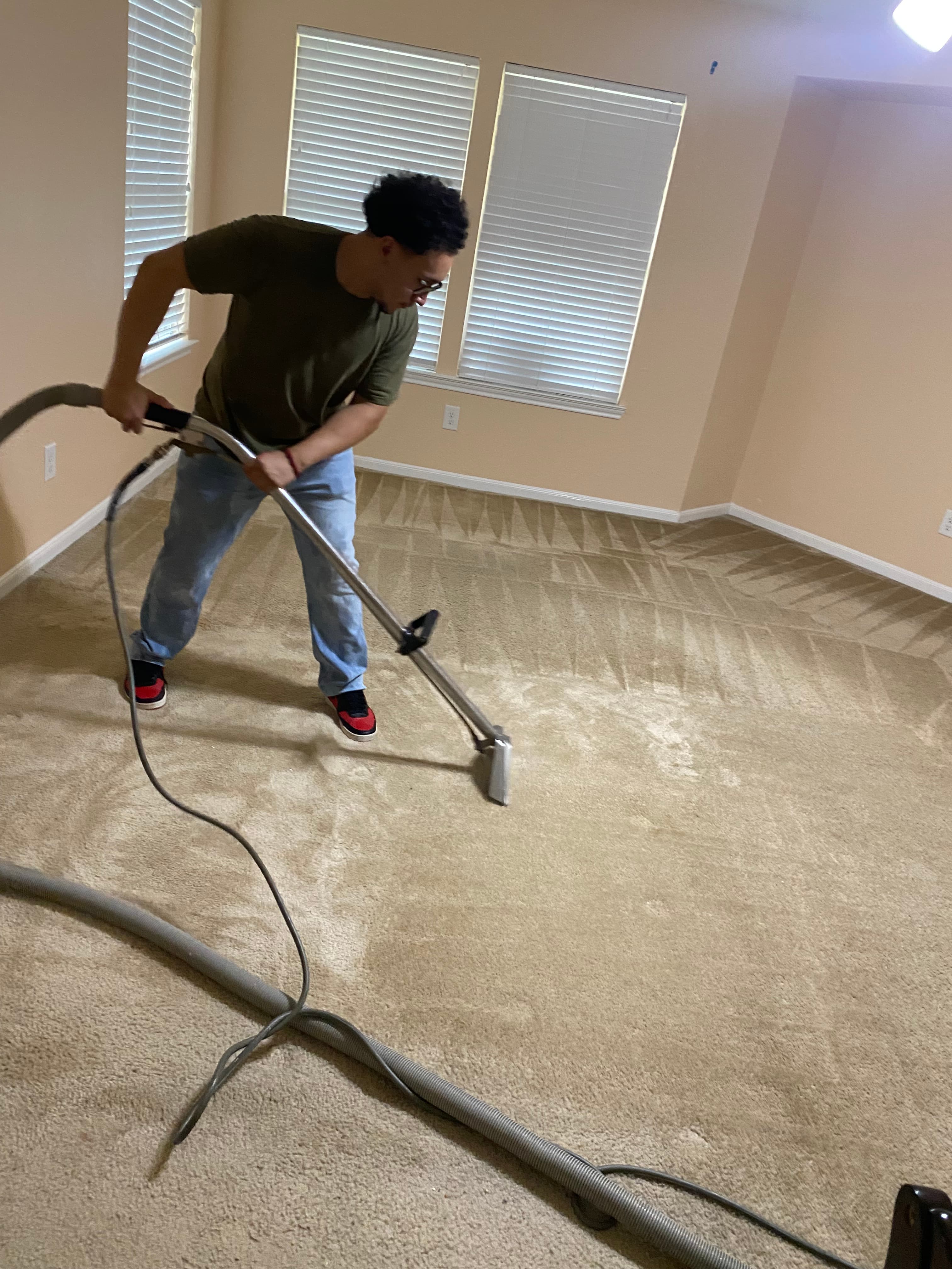 Man using a professional carpet cleaning wand on a beige carpet with visible cleaning patterns.